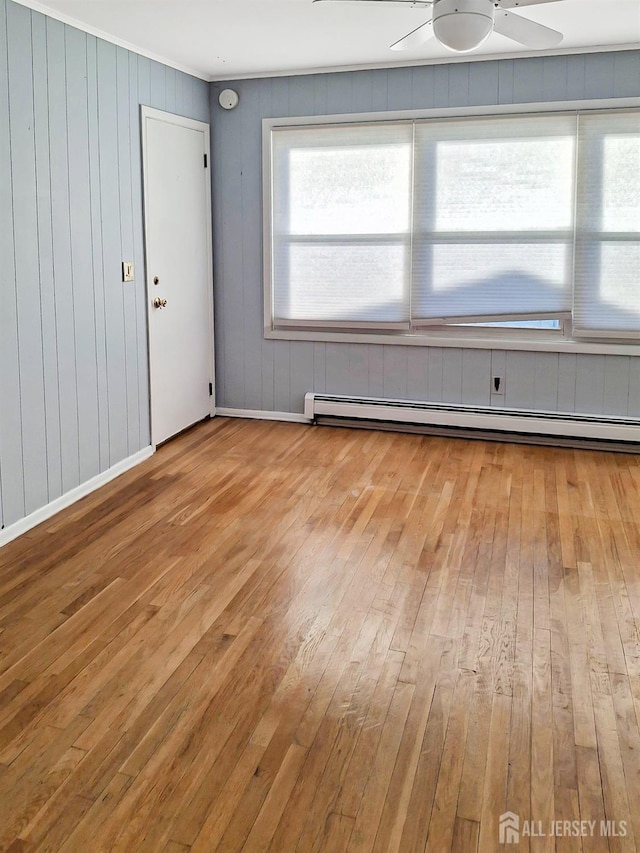 spare room featuring ceiling fan, light wood-type flooring, wooden walls, and a baseboard heating unit