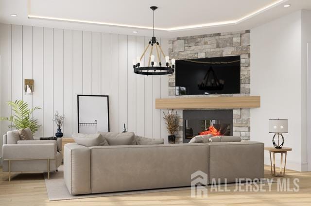 living room featuring a raised ceiling, light wood-type flooring, a fireplace, and a chandelier