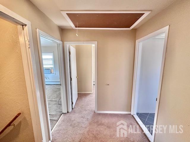 corridor featuring a baseboard radiator, baseboards, carpet, and attic access