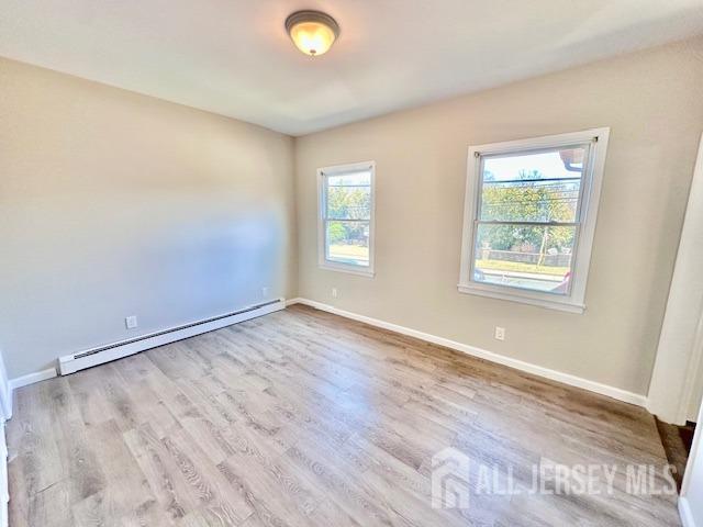 unfurnished room featuring a baseboard heating unit, wood finished floors, and baseboards