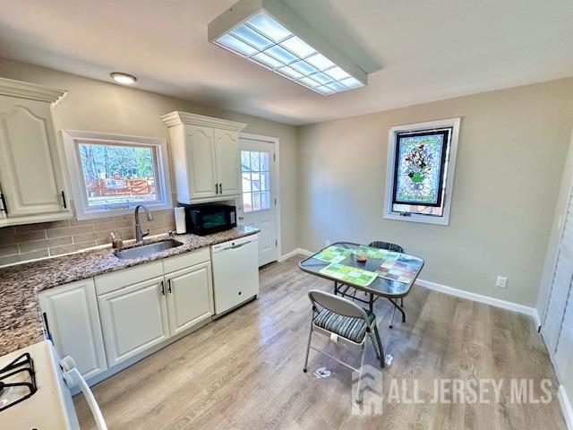 kitchen with white appliances, stone countertops, a sink, light wood-style floors, and white cabinetry