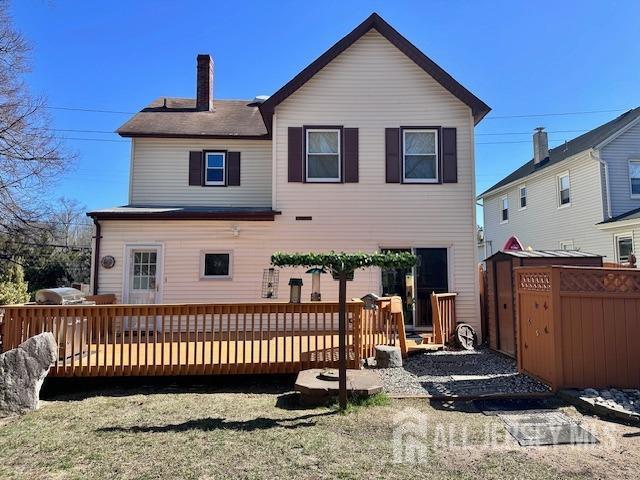 back of property featuring a wooden deck, a chimney, a storage shed, and an outdoor structure