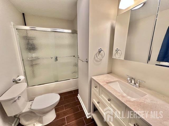bathroom featuring bath / shower combo with glass door, toilet, baseboards, wood tiled floor, and vanity