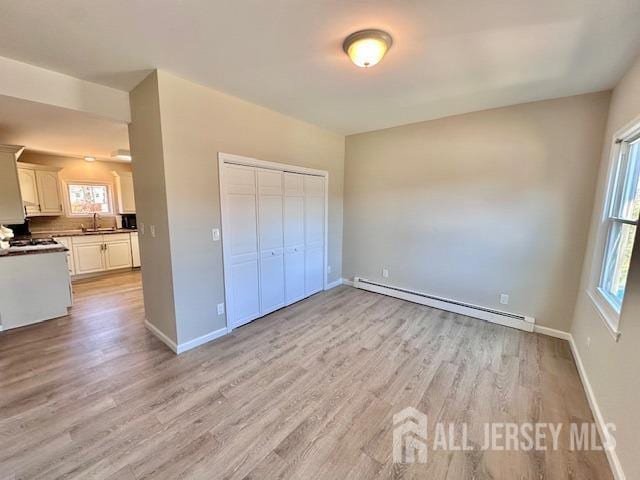 unfurnished bedroom featuring a baseboard heating unit, a sink, light wood finished floors, and multiple windows