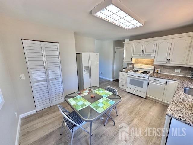 kitchen with light wood-style flooring, under cabinet range hood, backsplash, white cabinetry, and white appliances