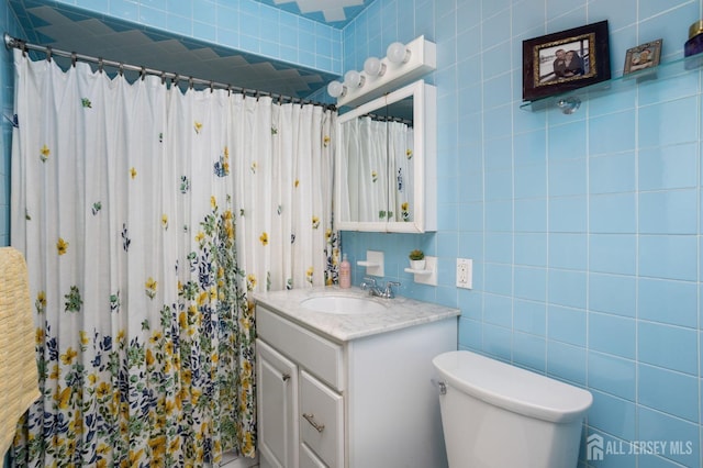 bathroom featuring toilet, a shower with shower curtain, vanity, and tile walls