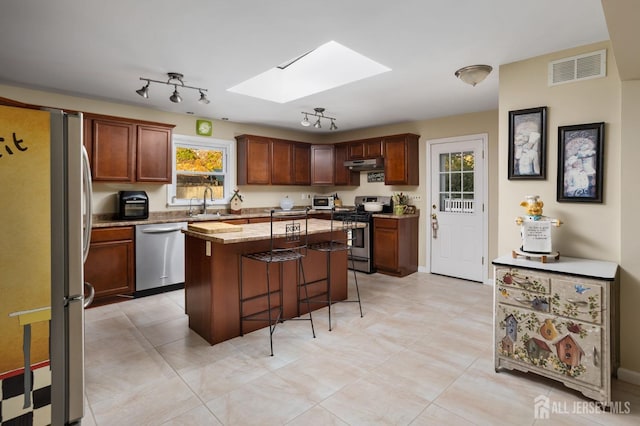 kitchen featuring light stone countertops, stainless steel appliances, a kitchen bar, a kitchen island, and a skylight