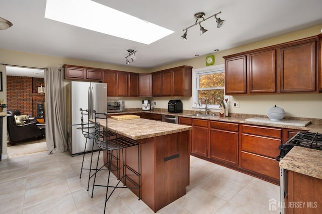 kitchen with a kitchen breakfast bar, stainless steel appliances, a skylight, a center island, and sink