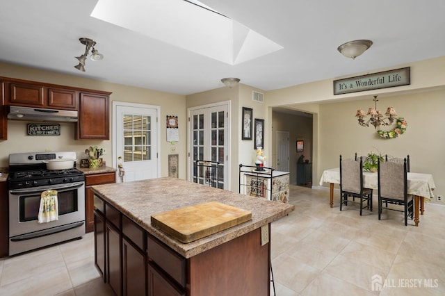 kitchen with a skylight, a center island, gas stove, light tile patterned floors, and an inviting chandelier