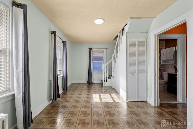 tiled entrance foyer featuring stairway, baseboards, and a textured ceiling