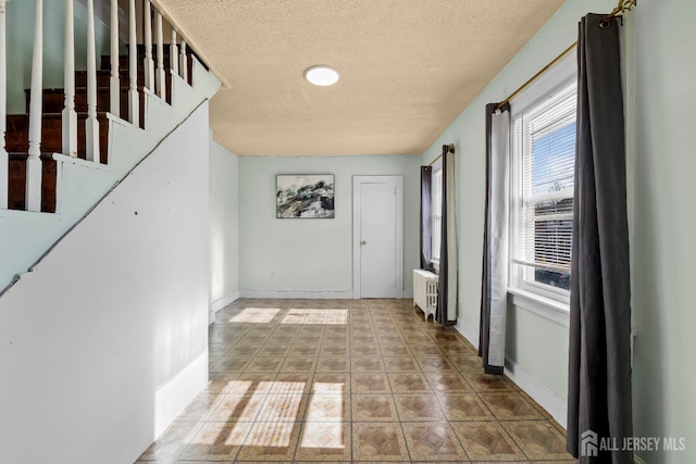 corridor with baseboards, radiator heating unit, stairs, a textured ceiling, and tile patterned floors