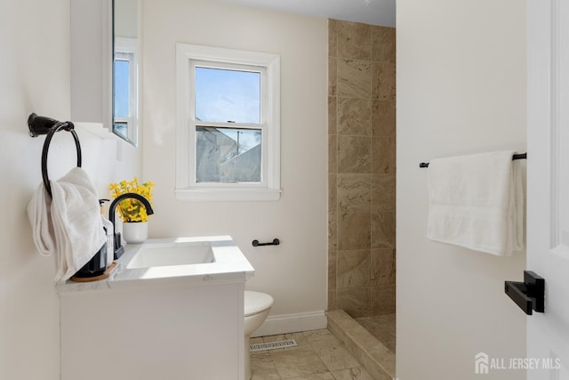 bathroom featuring vanity, a tile shower, and toilet