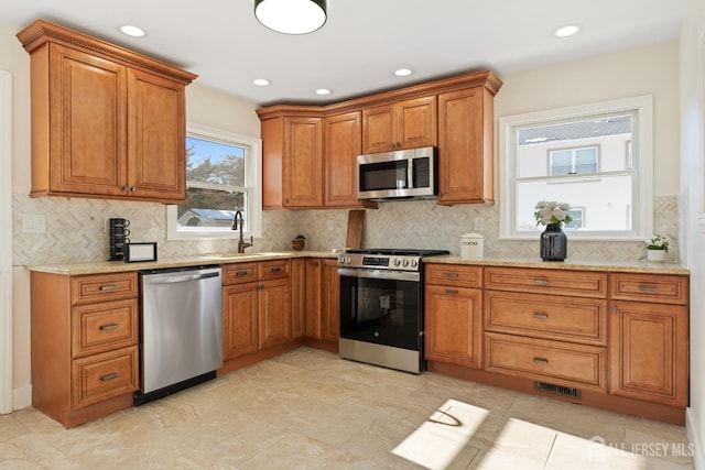 kitchen with sink, backsplash, light stone countertops, and appliances with stainless steel finishes