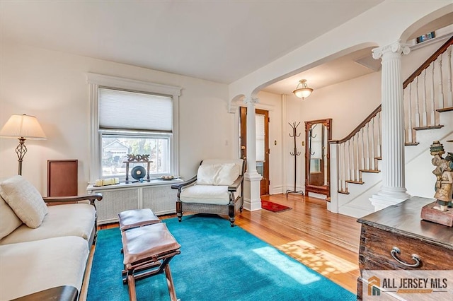 living room with wood finished floors, radiator heating unit, stairway, arched walkways, and decorative columns