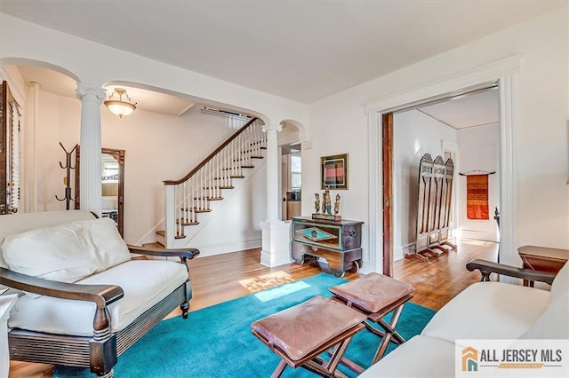 living area featuring arched walkways, stairs, ornate columns, and wood finished floors