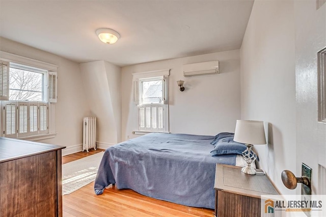 bedroom with a wall unit AC, radiator, wood finished floors, and baseboards