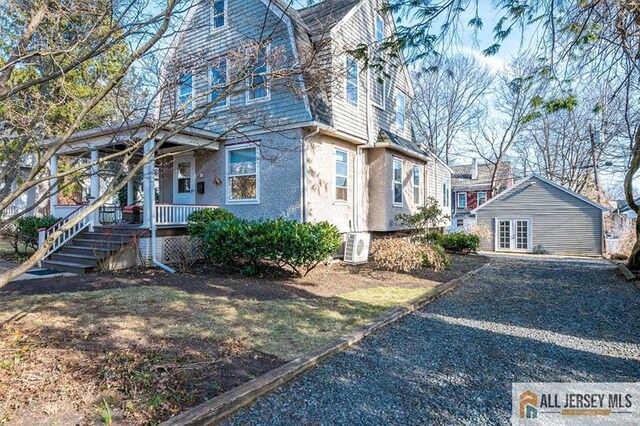 view of side of property featuring covered porch, french doors, a gambrel roof, and stucco siding