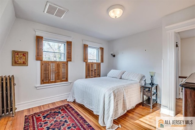 bedroom featuring visible vents, radiator, baseboards, and wood finished floors