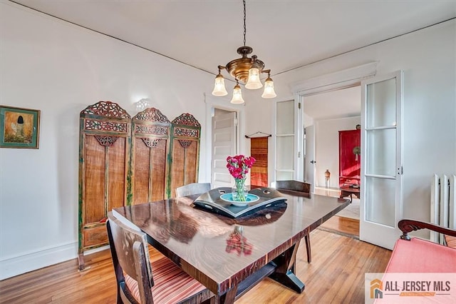 dining room with radiator heating unit, a notable chandelier, light wood-style floors, and baseboards