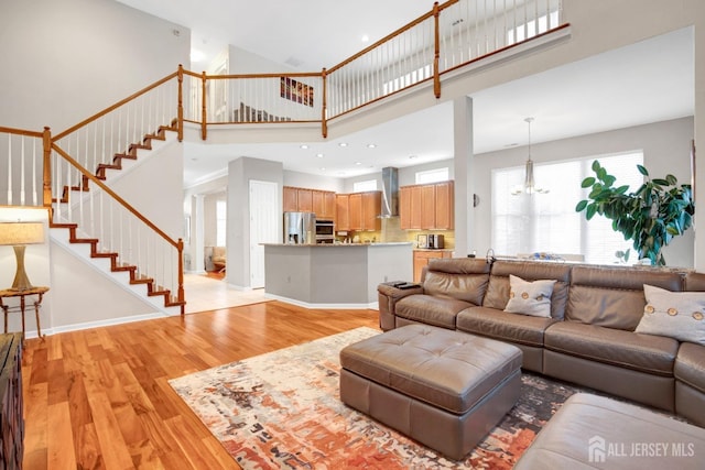 living area with stairway, light wood-style flooring, baseboards, a high ceiling, and a notable chandelier