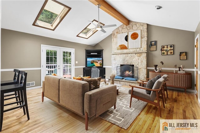 living room featuring ceiling fan, french doors, a stone fireplace, light hardwood / wood-style flooring, and vaulted ceiling with skylight