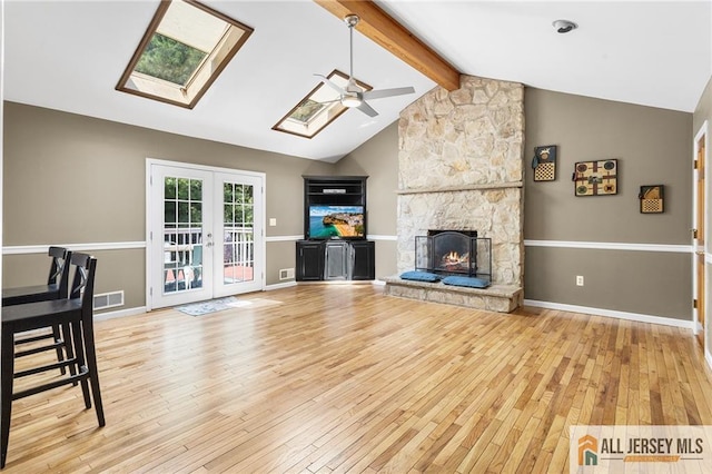 living room featuring ceiling fan, french doors, a stone fireplace, hardwood / wood-style floors, and vaulted ceiling with skylight