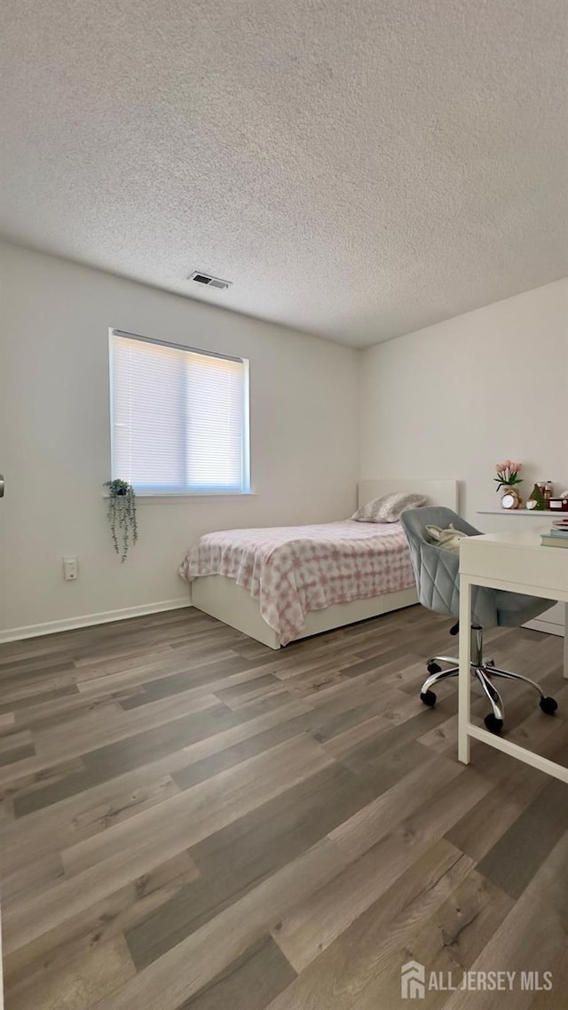 bedroom featuring baseboards, wood finished floors, visible vents, and a textured ceiling