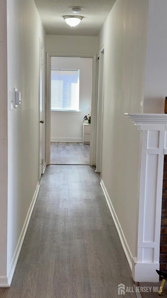 corridor featuring wood finished floors, baseboards, and a textured ceiling