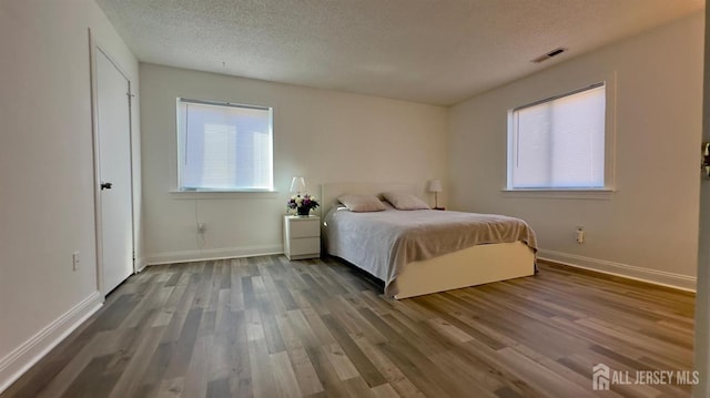 unfurnished bedroom featuring baseboards, wood finished floors, visible vents, and a textured ceiling