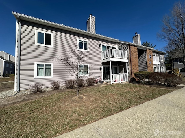 rear view of property featuring a lawn, a balcony, and a chimney