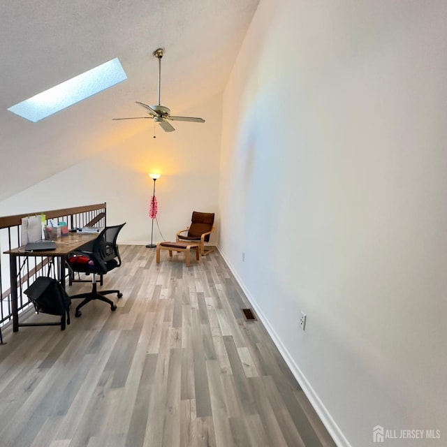 office featuring visible vents, baseboards, vaulted ceiling with skylight, wood finished floors, and a ceiling fan