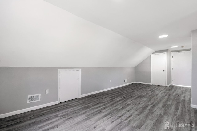 additional living space featuring dark wood finished floors, visible vents, baseboards, and lofted ceiling