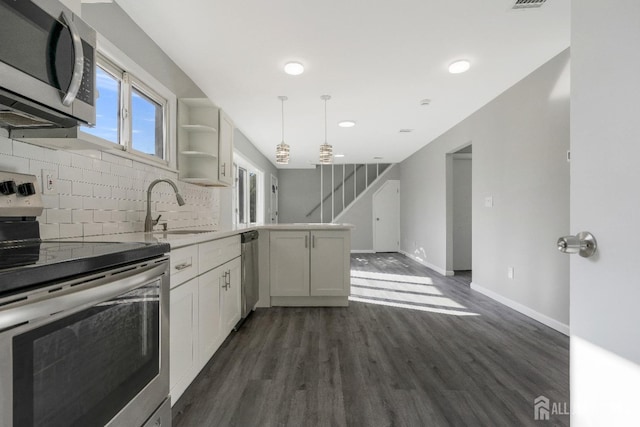 kitchen featuring dark wood-style floors, a peninsula, a sink, appliances with stainless steel finishes, and tasteful backsplash