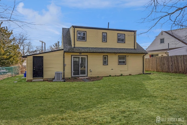 rear view of property featuring central AC unit, a lawn, fence, and a shingled roof