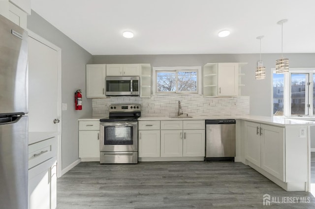 kitchen featuring open shelves, a peninsula, a sink, appliances with stainless steel finishes, and tasteful backsplash