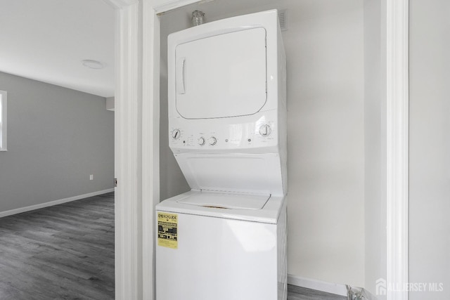 laundry room featuring laundry area, stacked washer / drying machine, baseboards, and wood finished floors