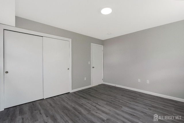 unfurnished bedroom with wood finished floors, baseboards, and a closet