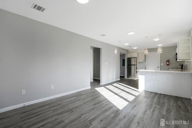 unfurnished living room with visible vents, a sink, baseboards, and dark wood-style flooring