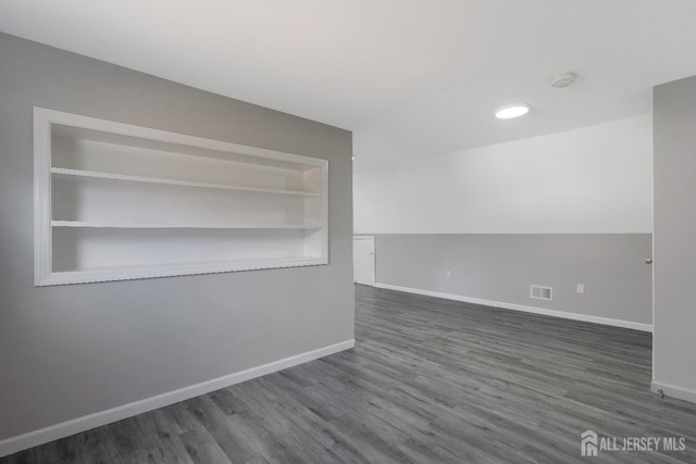 empty room with built in features, visible vents, baseboards, and dark wood-style floors