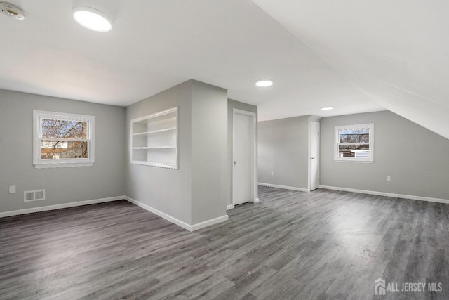 bonus room with visible vents, plenty of natural light, built in shelves, and dark wood-type flooring