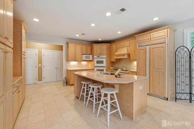 7 Pershing Ct, North Brunswick, NJ 08902 - kitchen with white appliances, a center island with sink, custom exhaust hood, light countertops, and light brown cabinetry