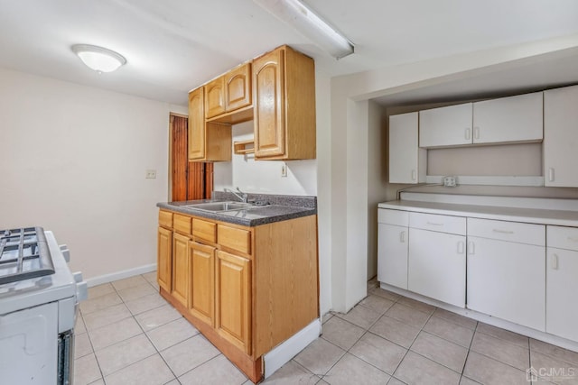 kitchen with a sink, light tile patterned floors, baseboards, and range with gas cooktop