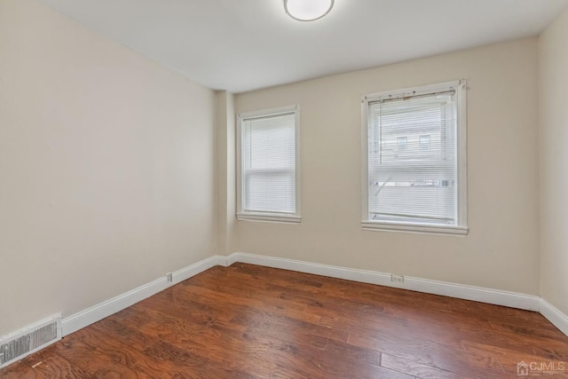 empty room with plenty of natural light, visible vents, baseboards, and wood finished floors