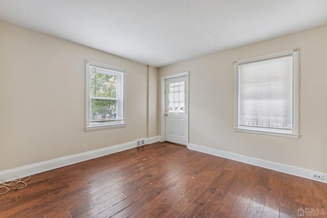 empty room featuring baseboards, dark wood-style floors, and visible vents