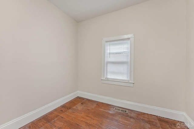 empty room featuring wood finished floors, baseboards, and visible vents