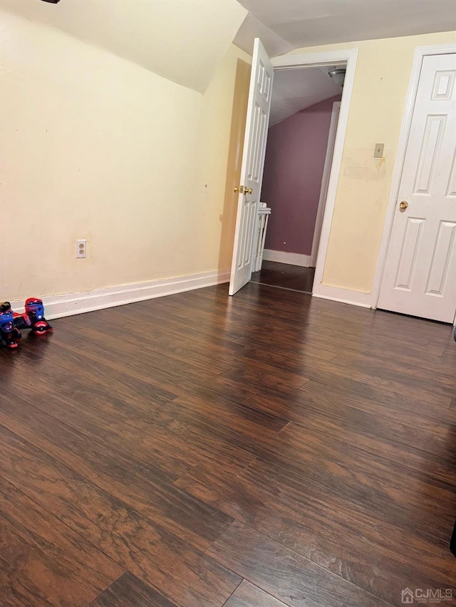 spare room featuring dark wood-style floors, vaulted ceiling, and baseboards