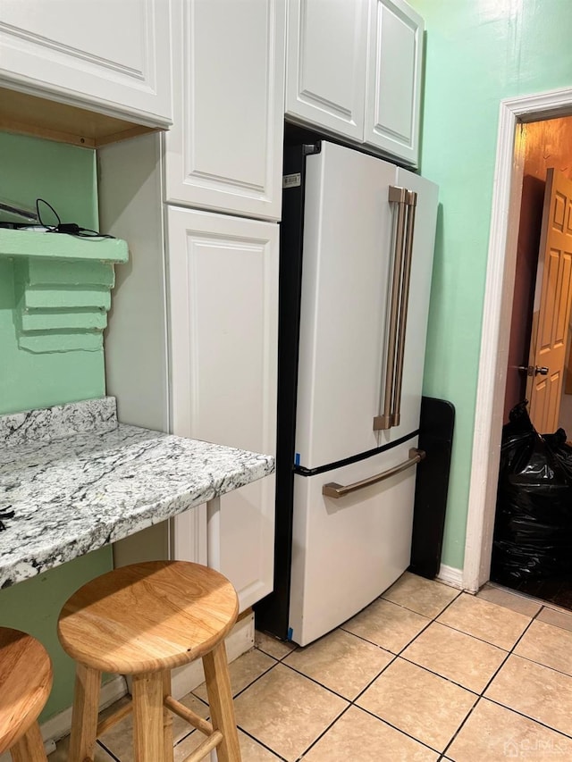 kitchen featuring high end refrigerator, light stone countertops, light tile patterned floors, and white cabinets