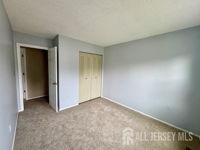 21 Rice Run, East Brunswick, NJ 08816 - unfurnished bedroom featuring carpet floors, a closet, baseboards, and a textured ceiling