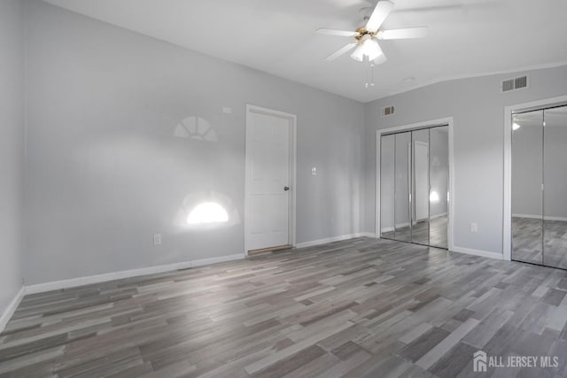 unfurnished bedroom with multiple closets, visible vents, baseboards, and wood finished floors