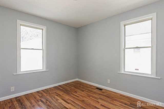 empty room featuring baseboards, visible vents, and wood finished floors